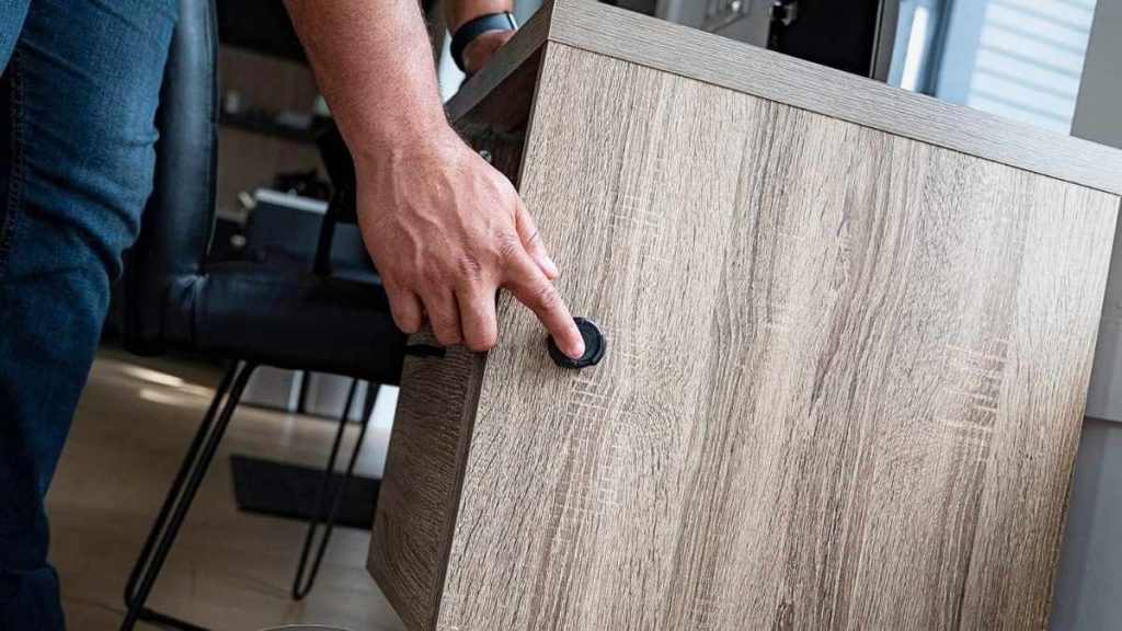 A close-up of a hand pressing a black button (Bluetooth Nano key 2.0) on a wooden cabinet, showcasing modern home furniture interaction.